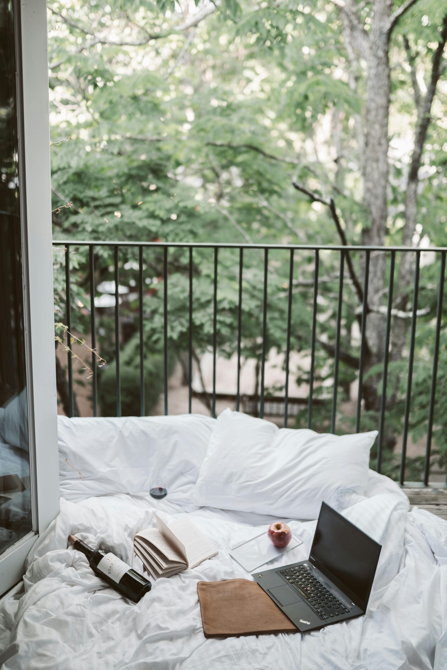 Relaxing on a cozy balcony with a laptop and wine bottle, surrounded by lush greenery.